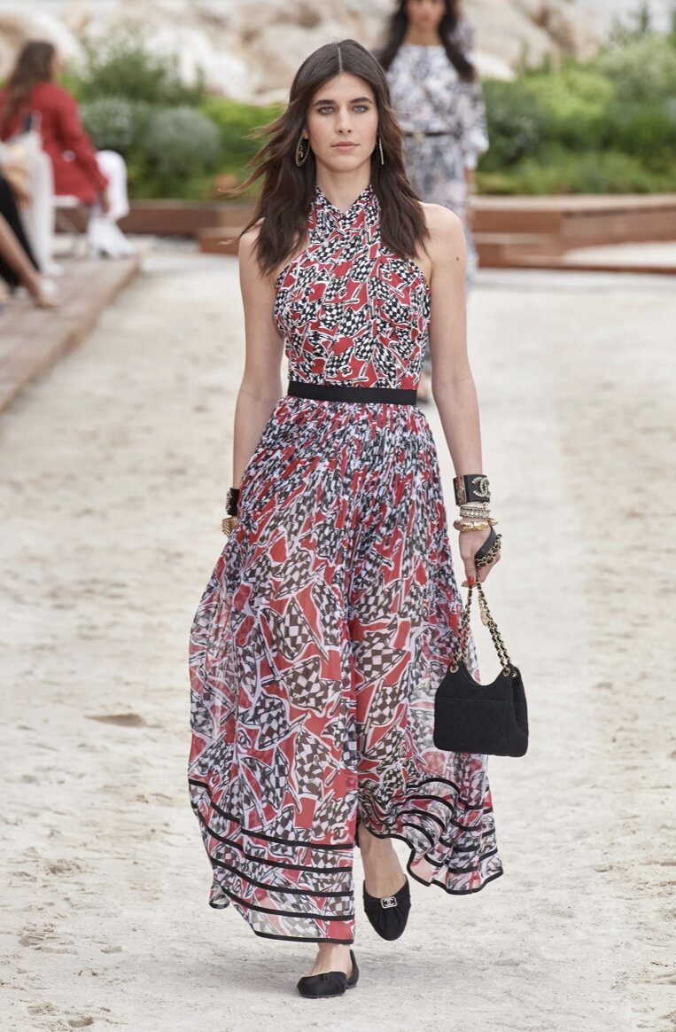 Woman in a flowy halterdress with racing flags in black and red at the Chanel cruise 2023 Show | Ode2style.com