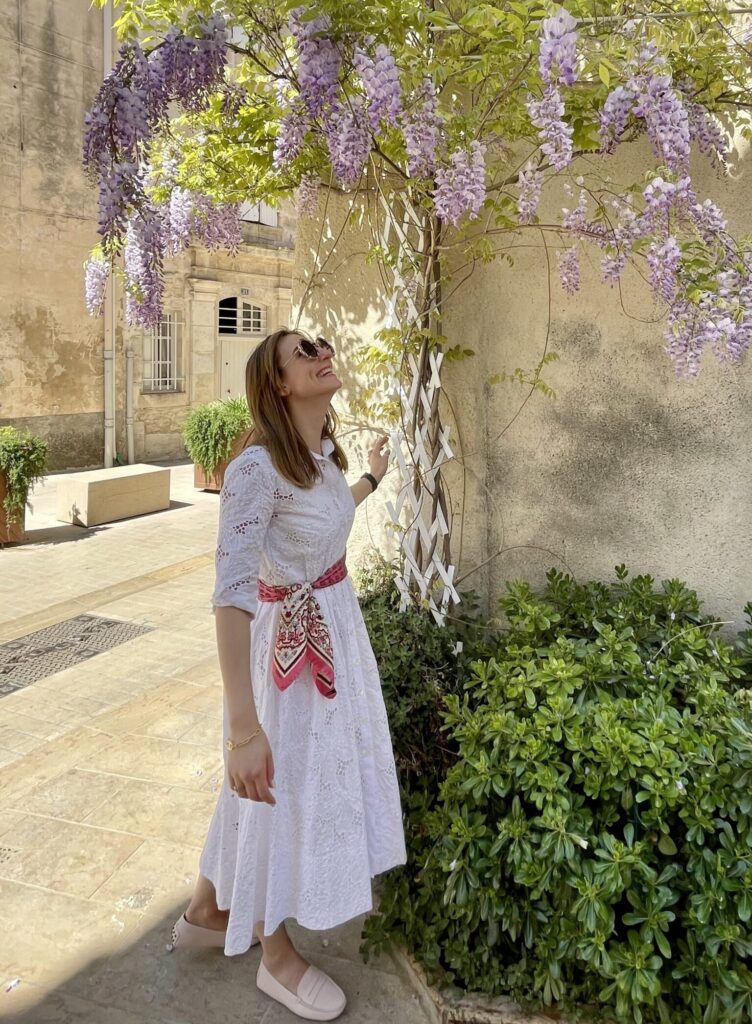 Astrid in a white embroidered dress looking at flowers in the Provence, France | Ode2style.com