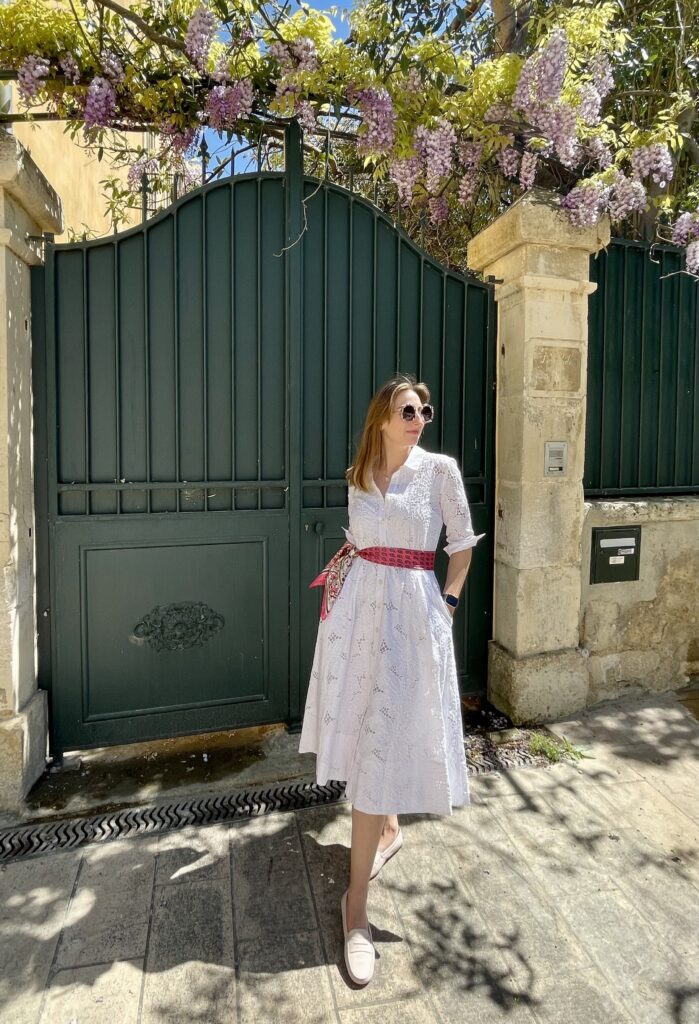 Astrid in front of a flower covered gate in a white dress from Souleiado with a pink scarf around the wast and blush pink Tod loafers | Ode2style.com