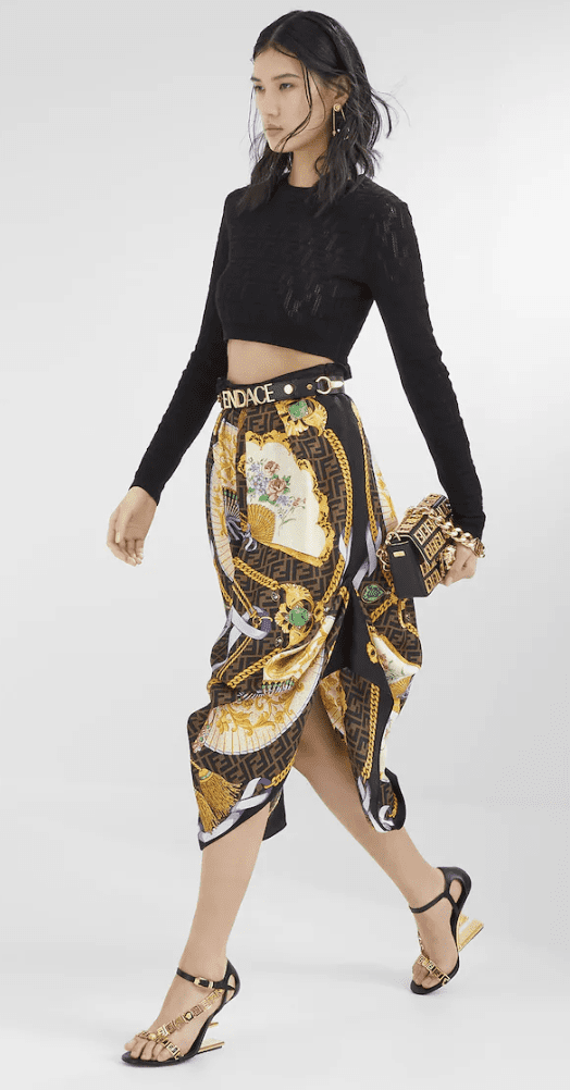 Model wearing a black long sleeved crop top and a gold printed flowy high waisted skirt with highed heeled sandals | Ode2style.com
