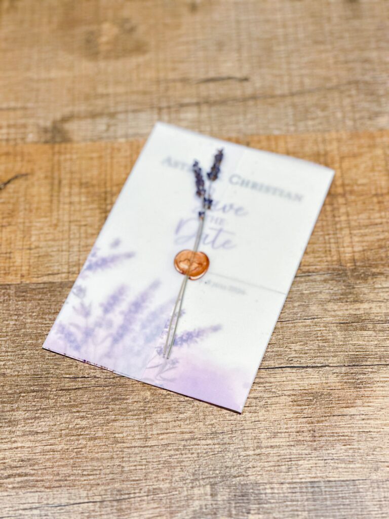 Wedding save-the-date with lavender imagery, a candle wax stamp and 2 lavender branches atop a wooden table