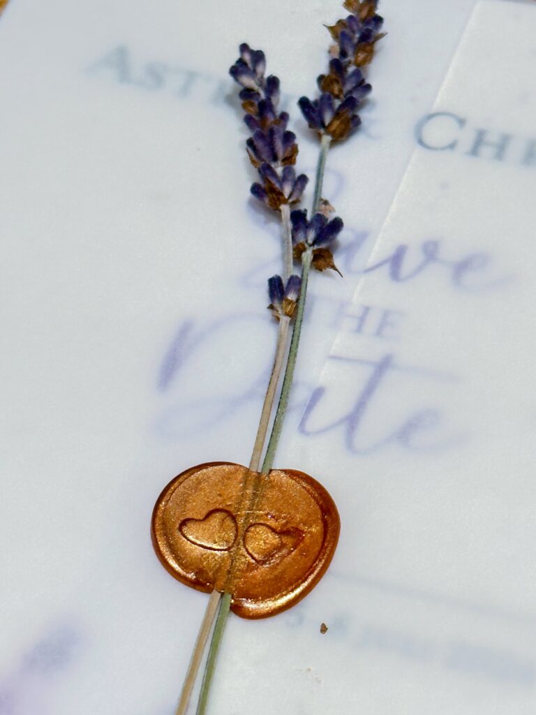 A close-up shot of a wedding save-the-date with a tracy paper and a copper candle wax stamped adorned with two lavender branches